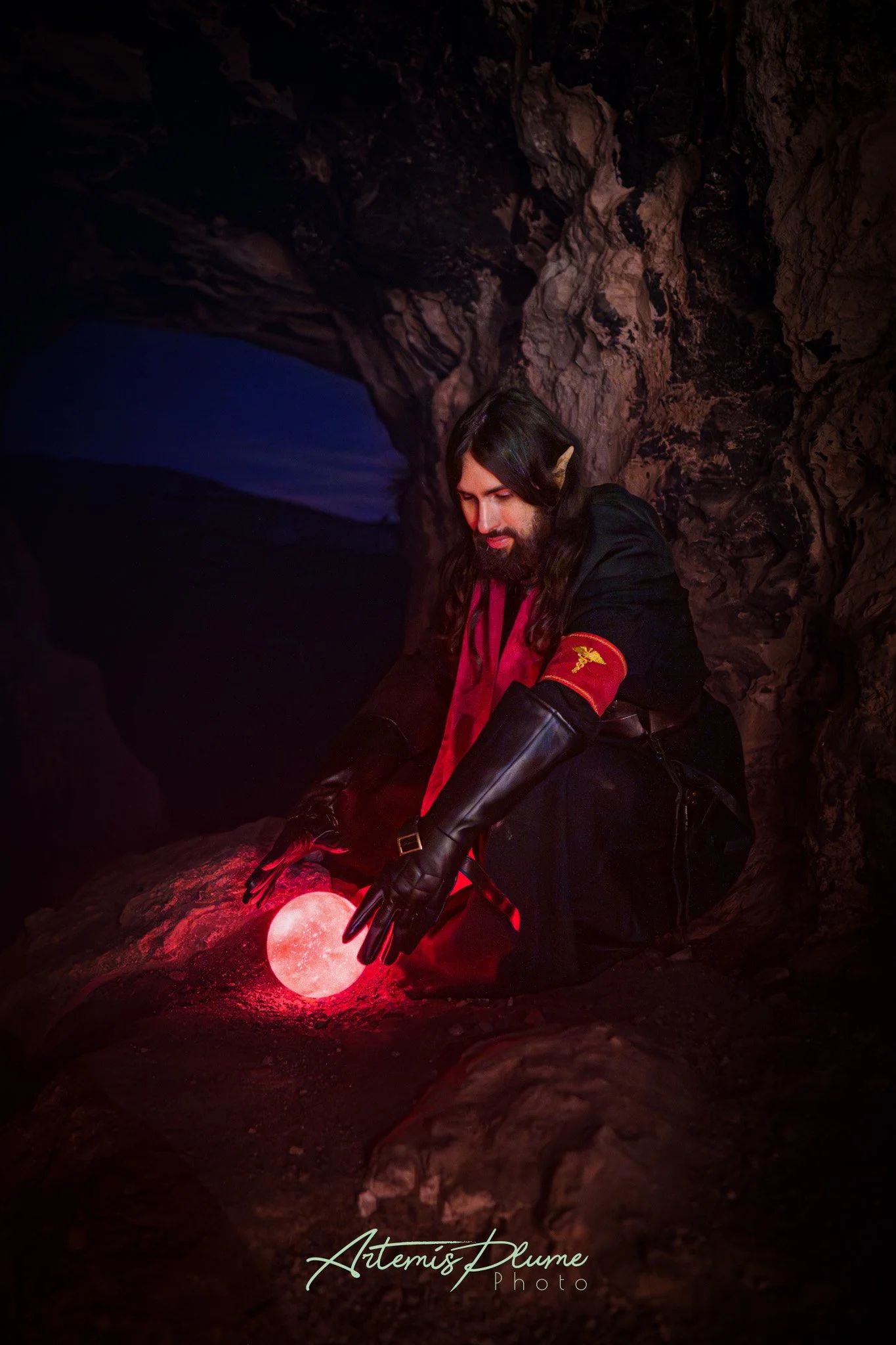 Photo d'un homme en costume d'elfe noir, assis face à une boule lumineuse