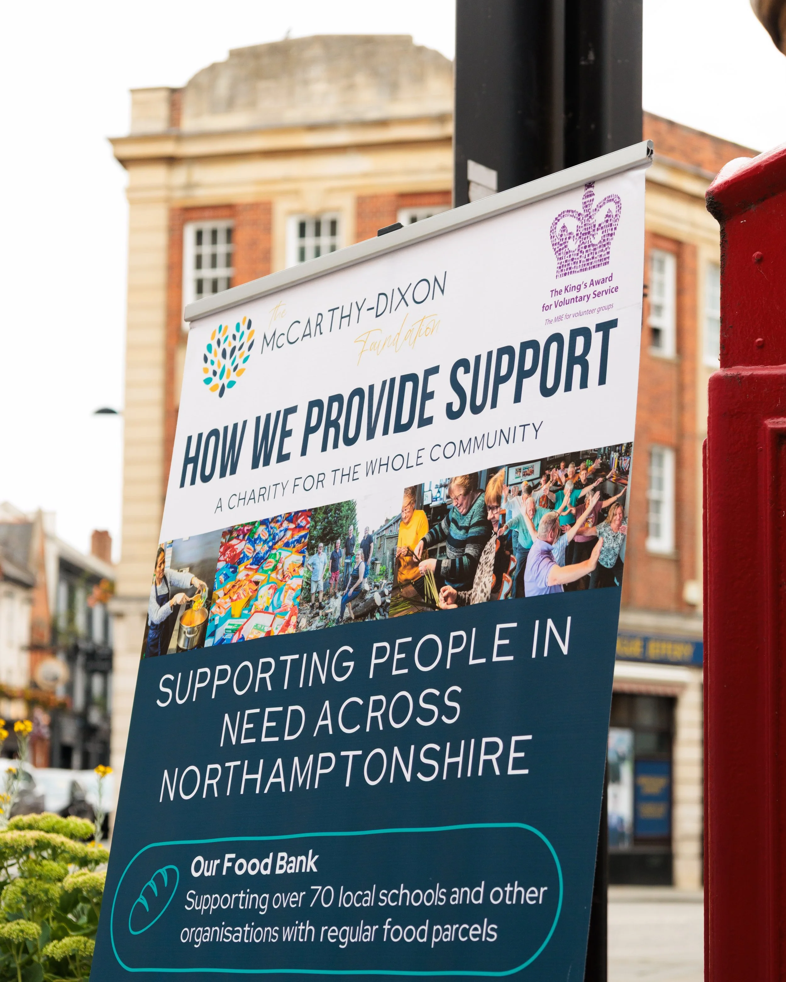 Signboard for McCarthy-Dixon Foundation describing charitable support activities for the community in Northamptonshire, including food bank services supporting local schools and organizations.