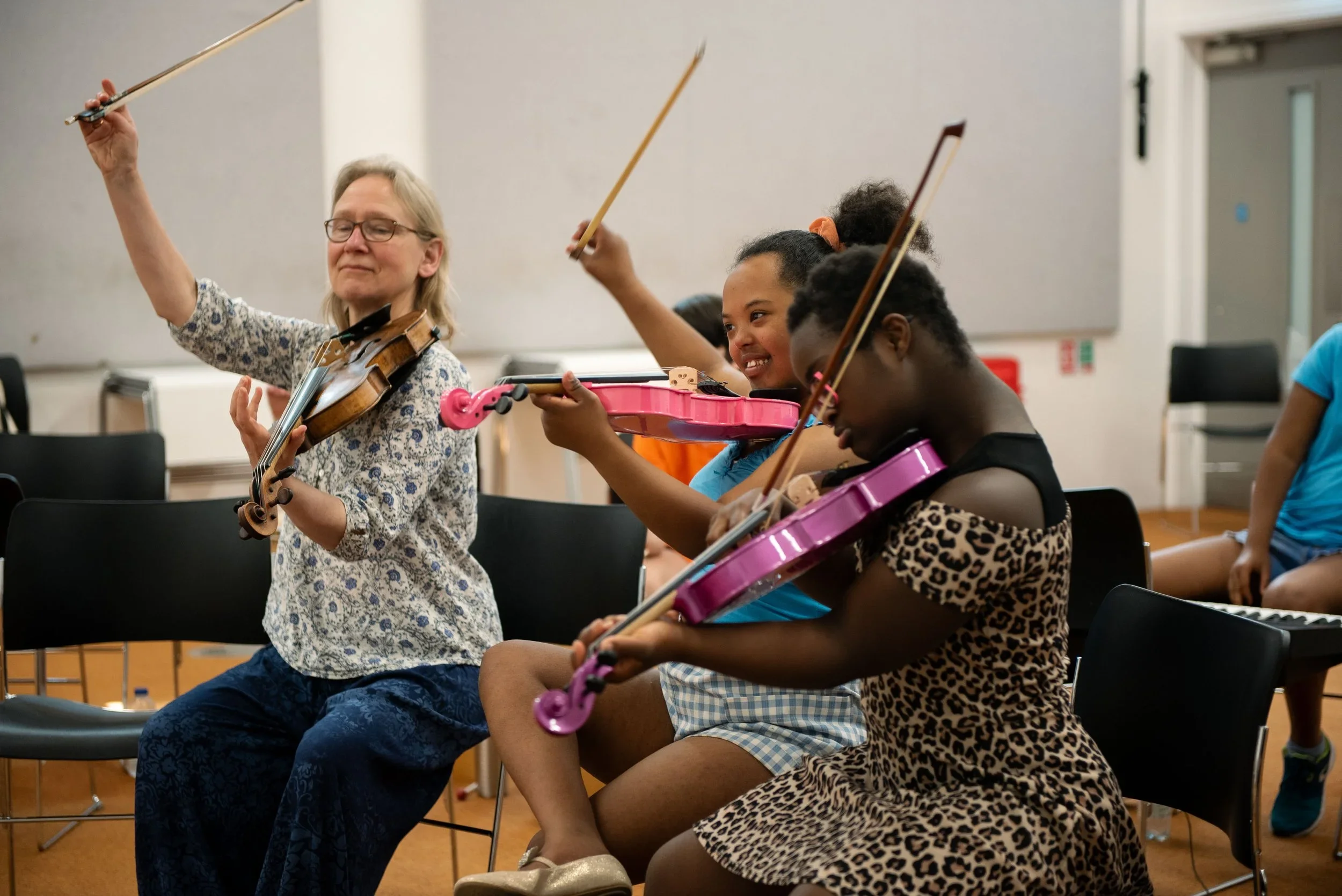 The image shows participants playing the violin with an instructor