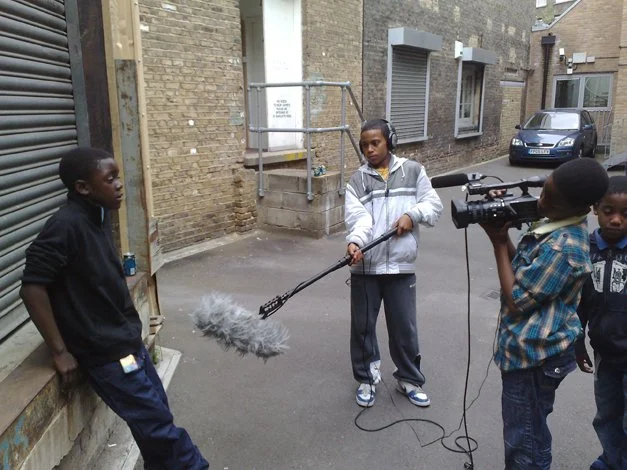 The image shows a group of young people recording a film or similar with a camera and sound equipment