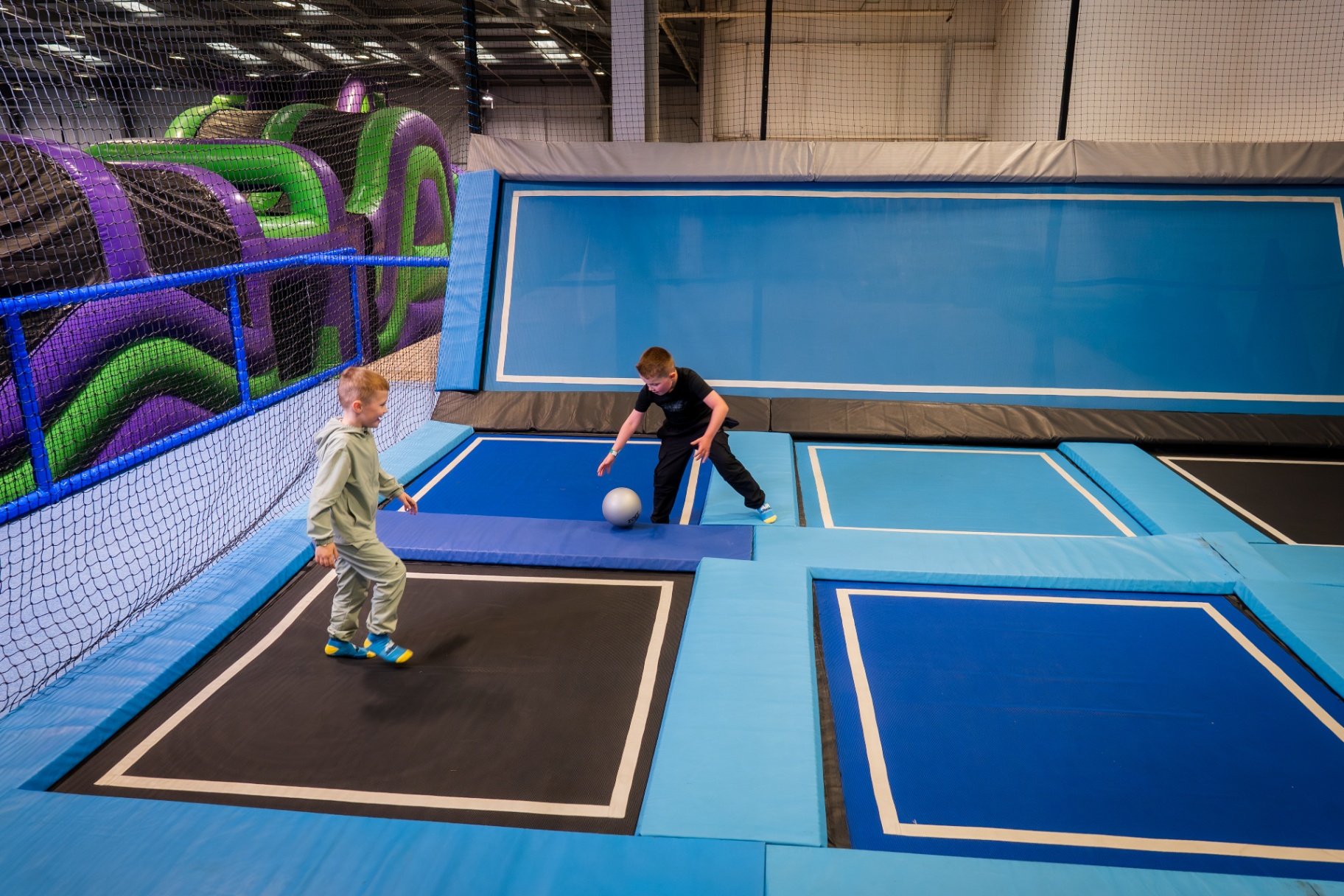 The image shows two children playing dodgeball on the trampolines