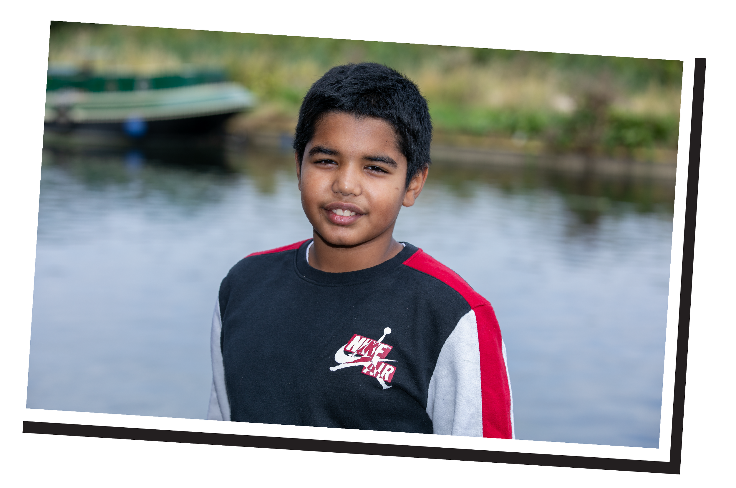 A young man smiling at the camera and enjoying a day at the lake