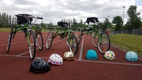 The image shows three adapted trikes and colourful helmets