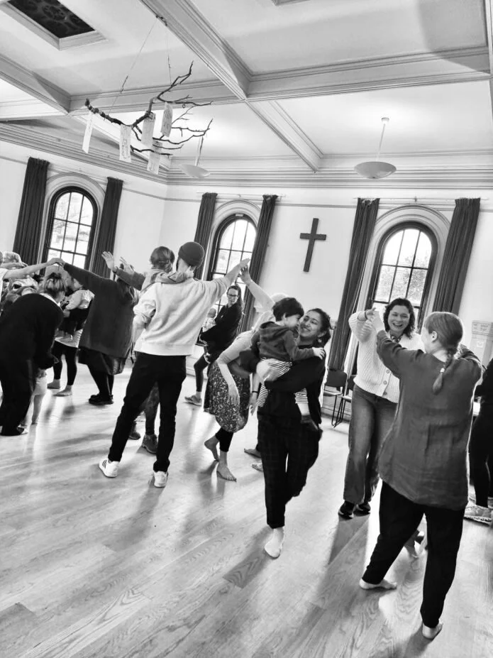 The photo is in black and white and shows families and children dancing in a hall