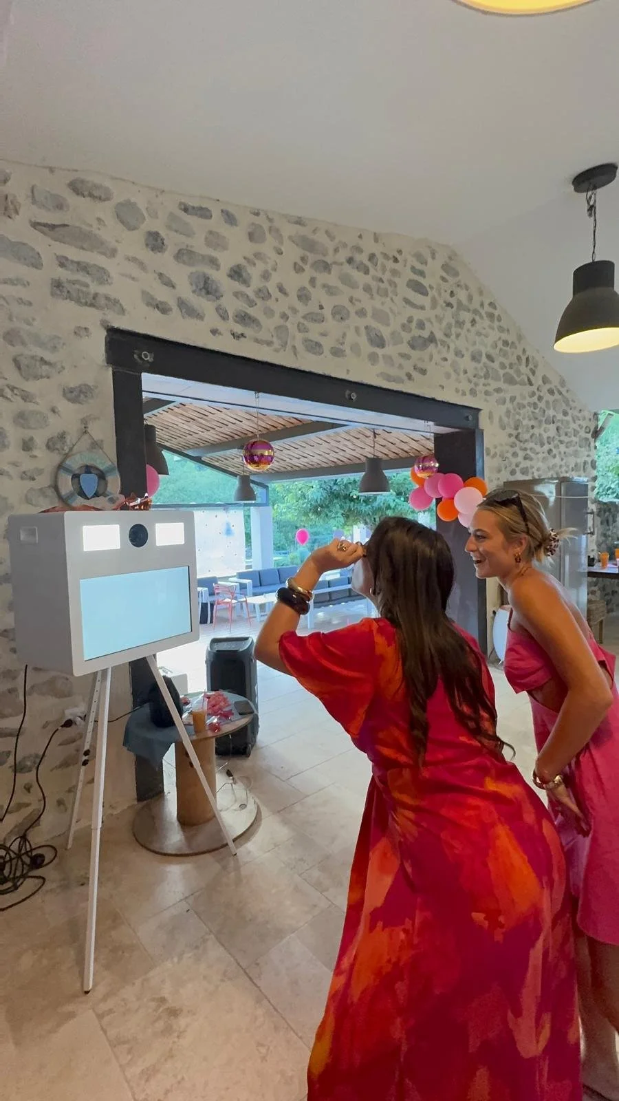 location de photobooth interactif dans une salle avec décoration pour anniversaire. Des invités prennent la pose devant le photobooth avec des accesoires.