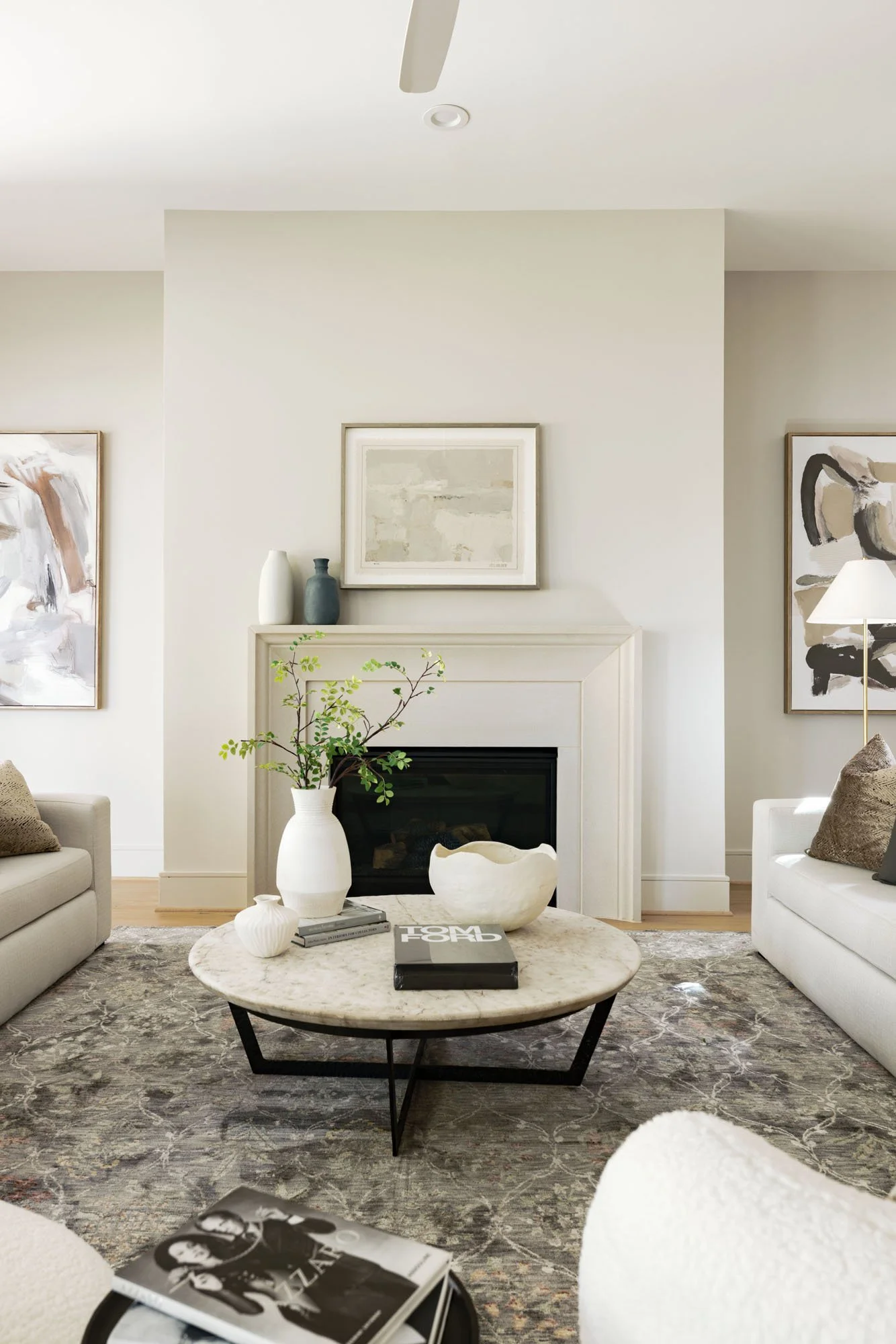 Cast stone fireplace framed by neutral abstract art with a round marble coffee table and cream sofas