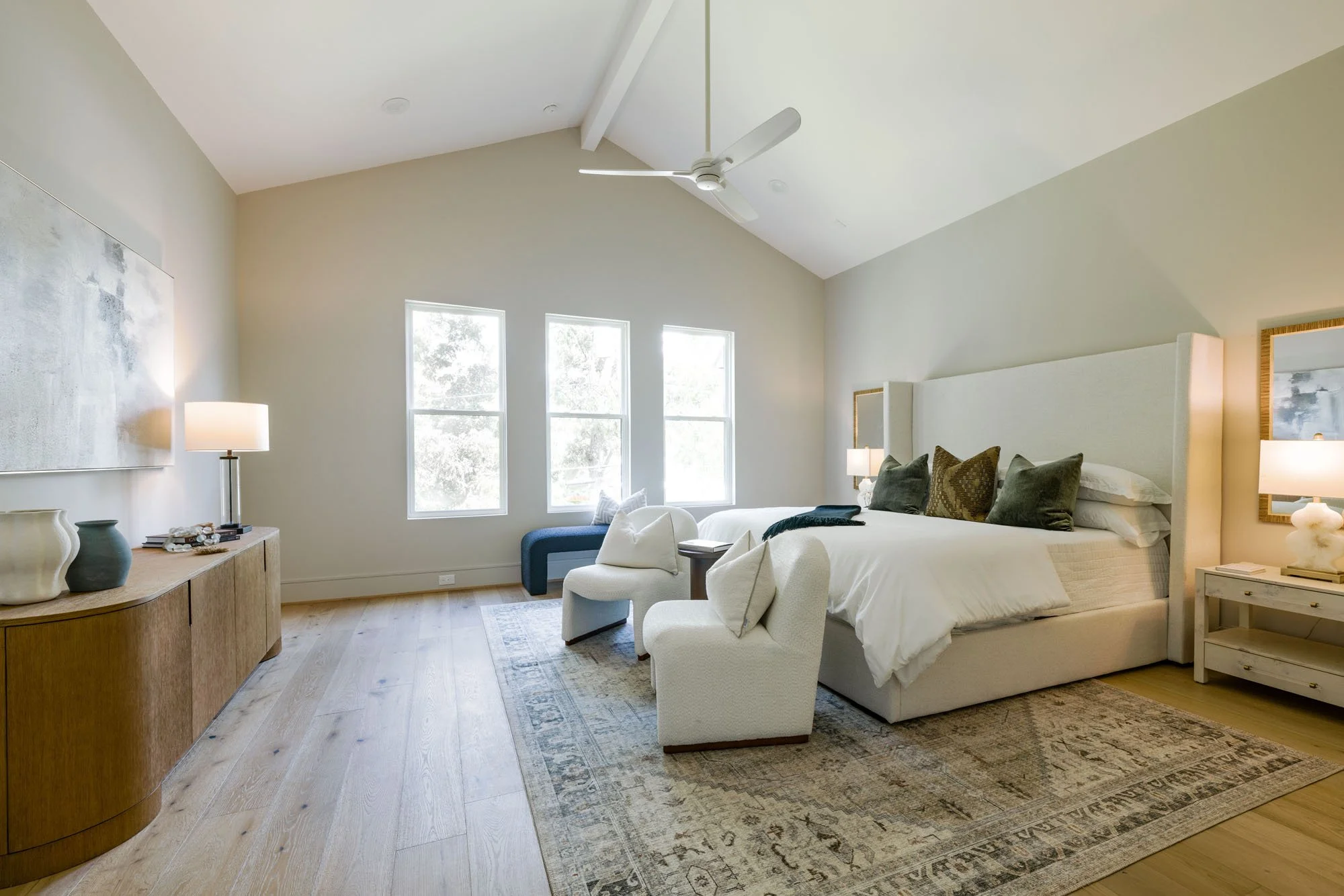 Primary bedroom with vaulted beamed ceiling, upholstered wingback bed, and bouclé accent chairs
