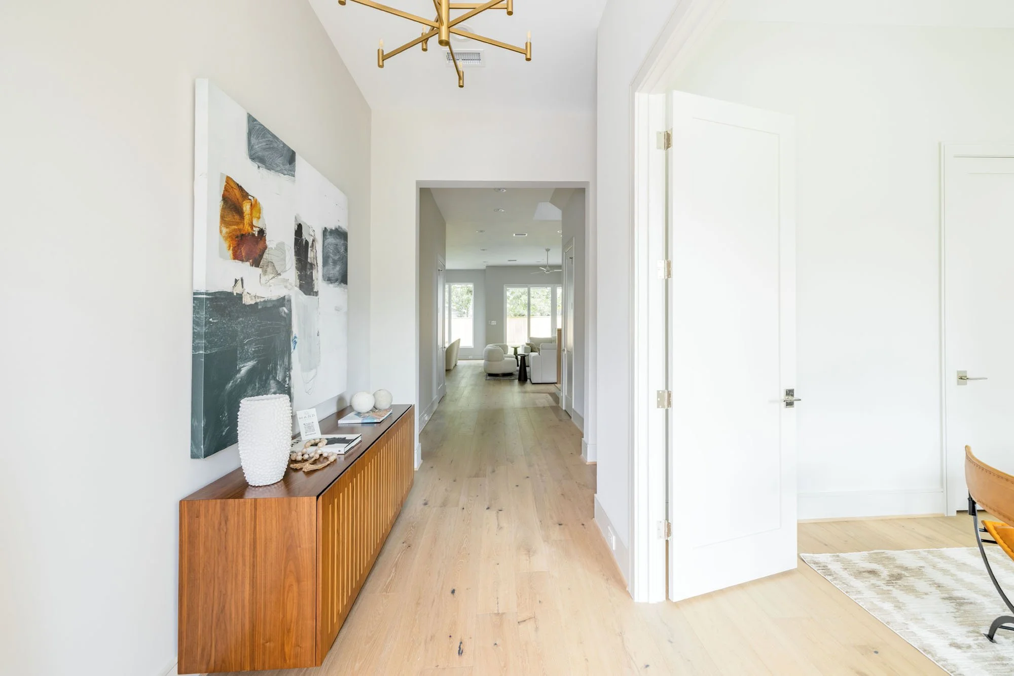 Long entry hall with wide-plank white oak floors and brass chandelier opening to the living room