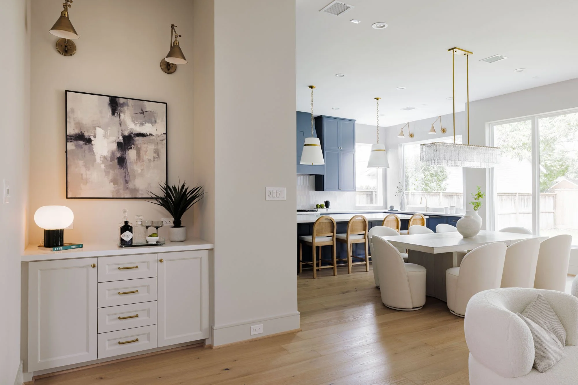 Built-in dry bar with brass sconces beside an open navy blue kitchen and dining area