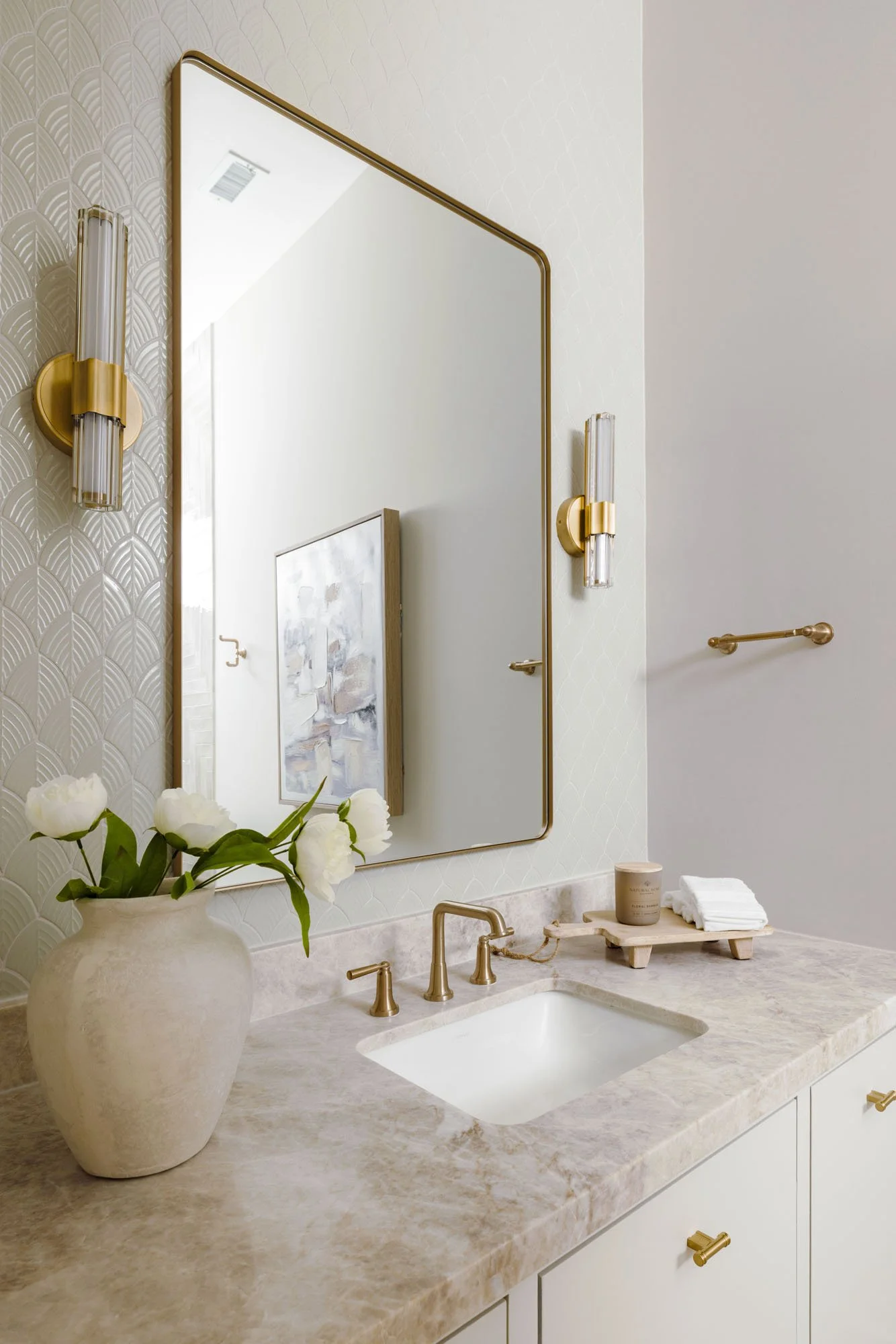 Powder bath with quartzite vanity top, brushed gold faucet, brass sconce, and white cabinetry