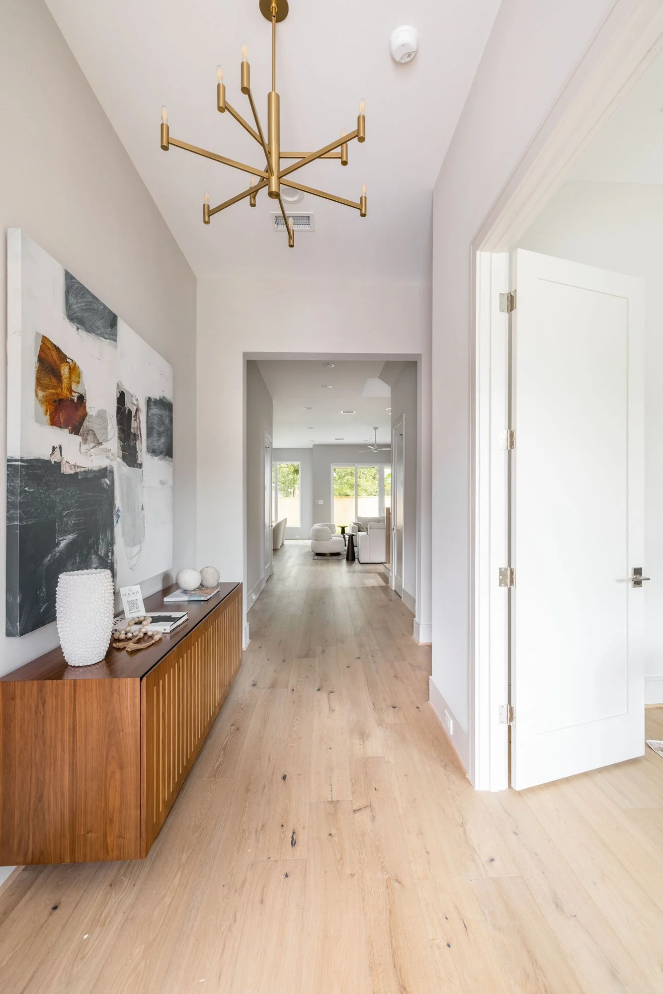 Bright foyer with walnut floating credenza, abstract art, and gold chandelier leading to the open living area