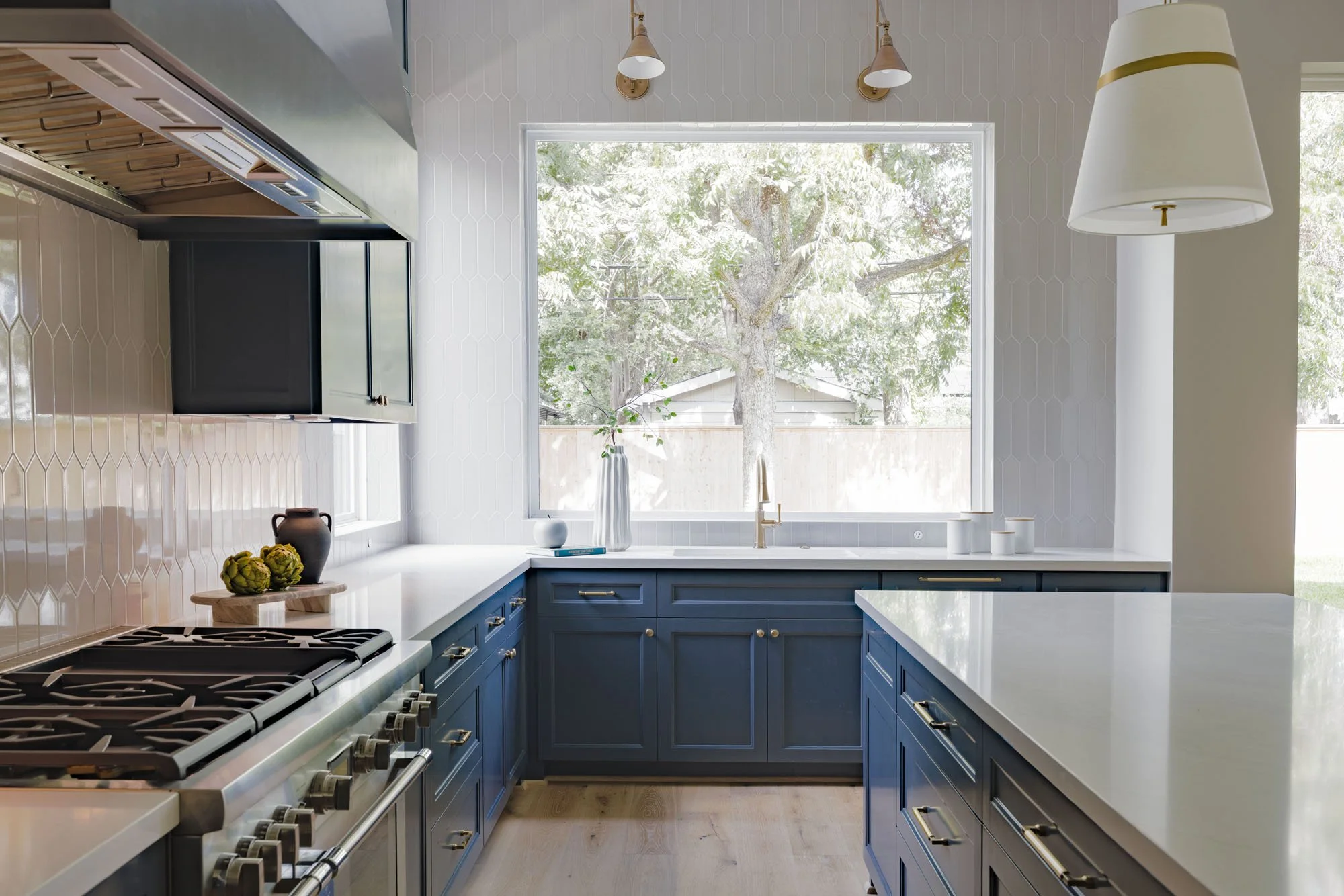 Chef’s kitchen with gas range, navy cabinets, white picket tile, and large picture window over the sink