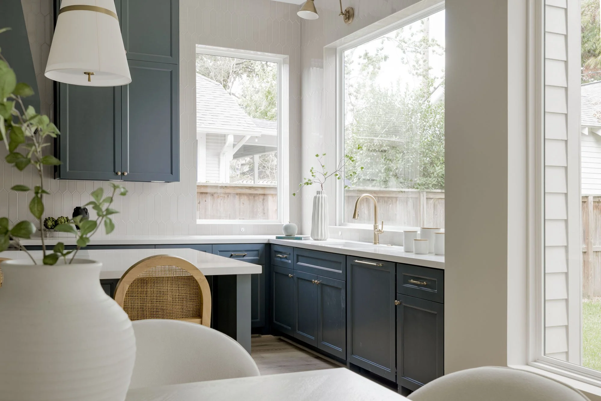 Navy shaker kitchen cabinets with picket tile backsplash, gold faucet, and corner windows over the sink