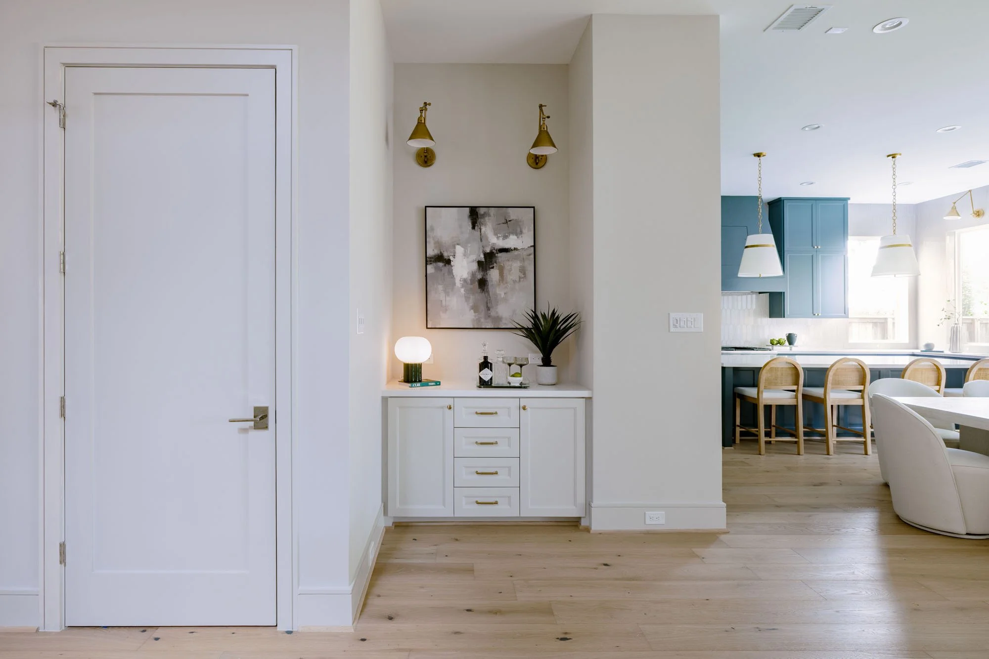 White dry bar nook with brass swing-arm sconces and gold hardware next to the open kitchen