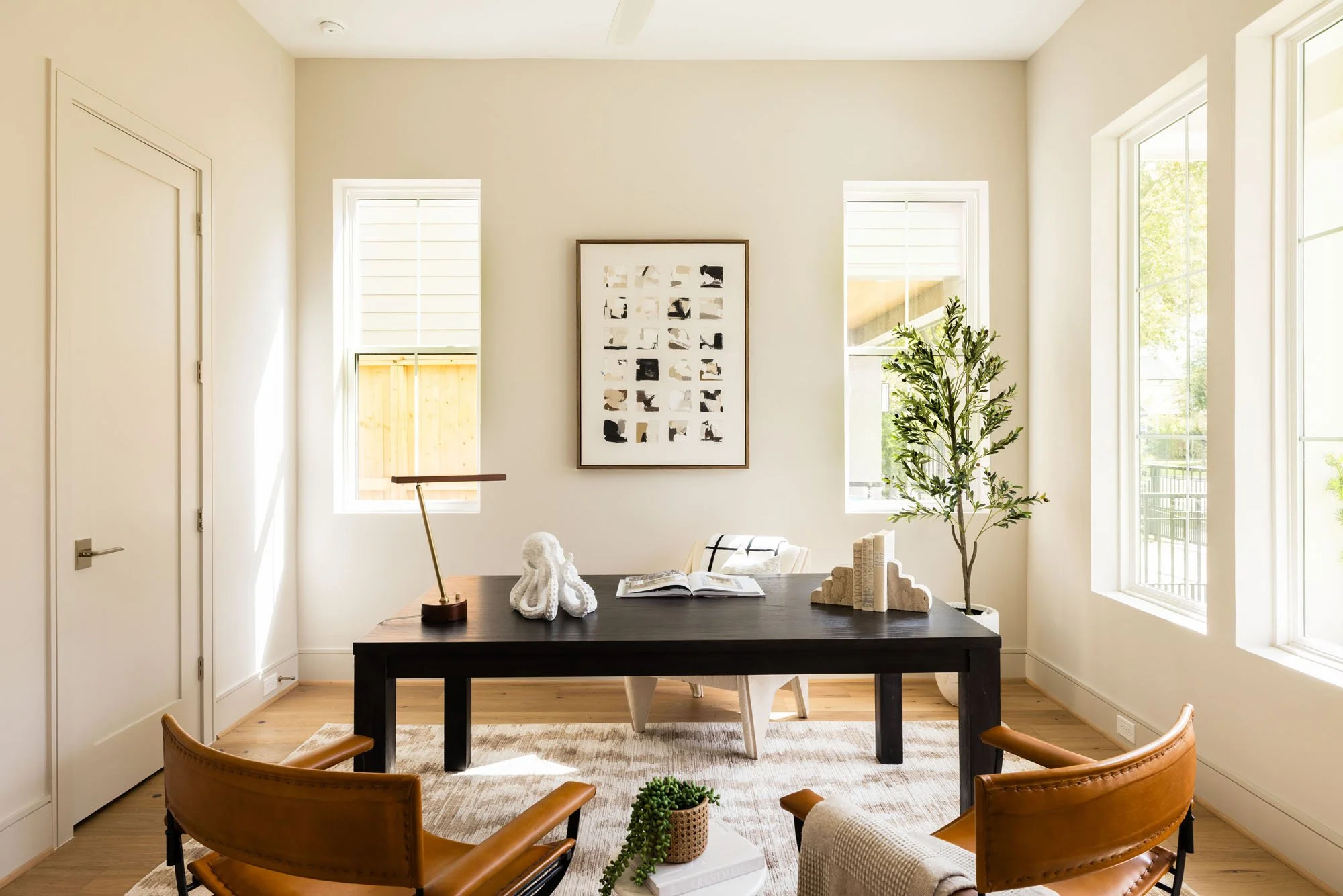 Sunlit home office with dark wood desk, cognac leather chairs, and tall windows in a transitional farmhouse