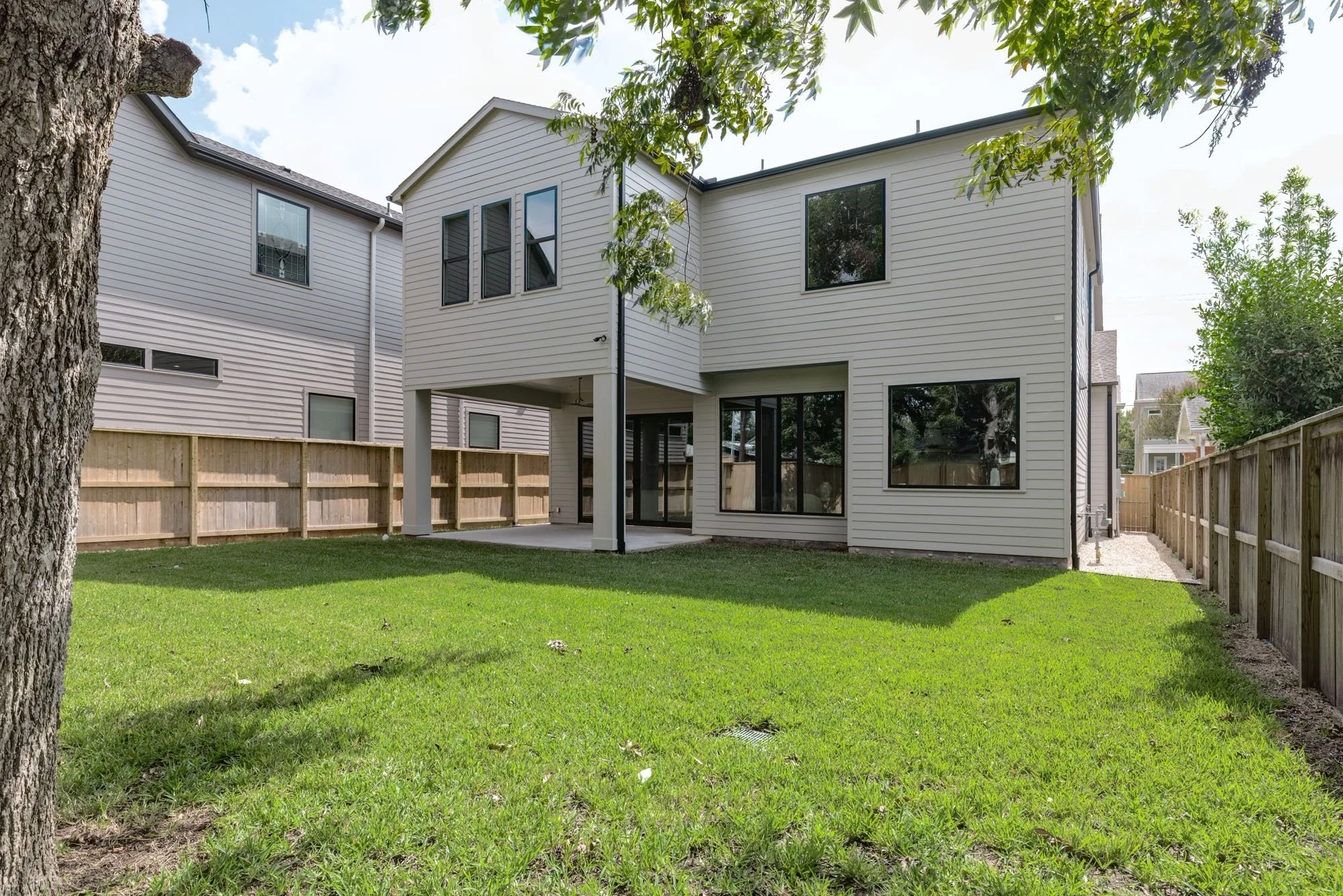 Fenced backyard with large lawn, mature shade tree, and covered patio of a transitional farmhouse