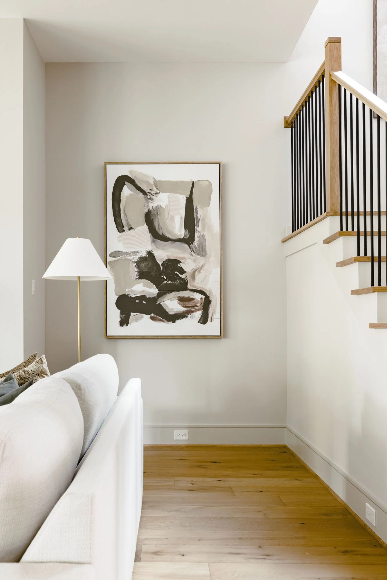 Living room corner with abstract art, brass floor lamp, and oak staircase with black iron balusters