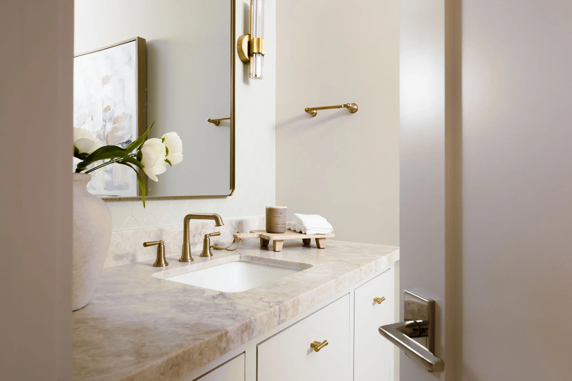 Powder bath with scalloped tile wall, brass-framed mirror, crystal sconces, and quartzite vanity