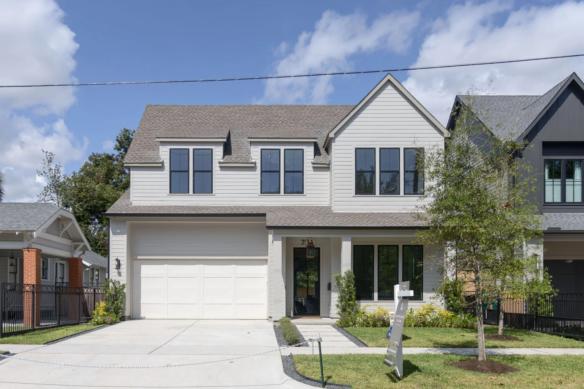 Transitional farmhouse spec home with gray lap siding, black windows, dormers, and a two-car garage at 711 12th St.