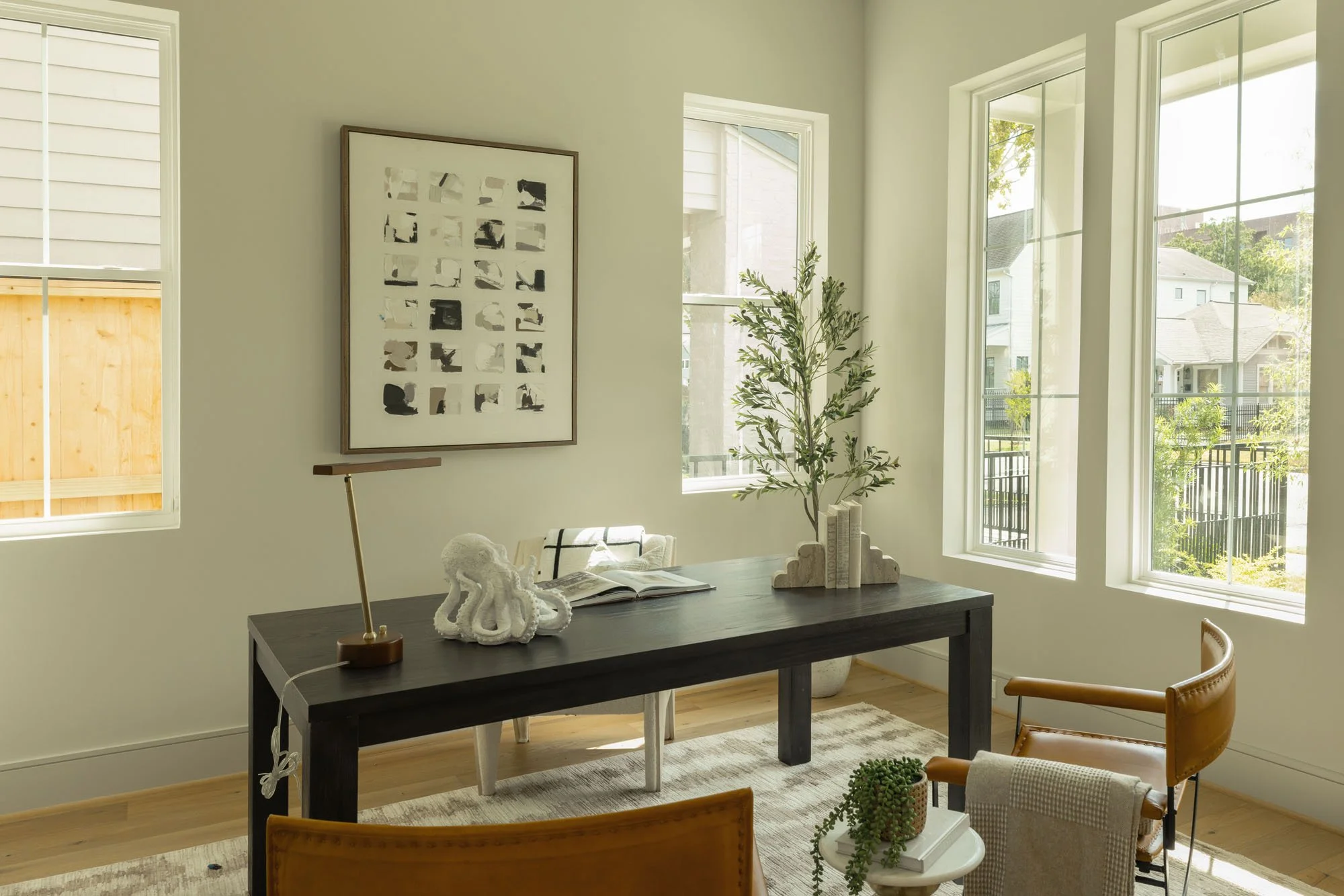 Home office with dark wood desk, leather armchairs, and tall windows overlooking a tree-lined street