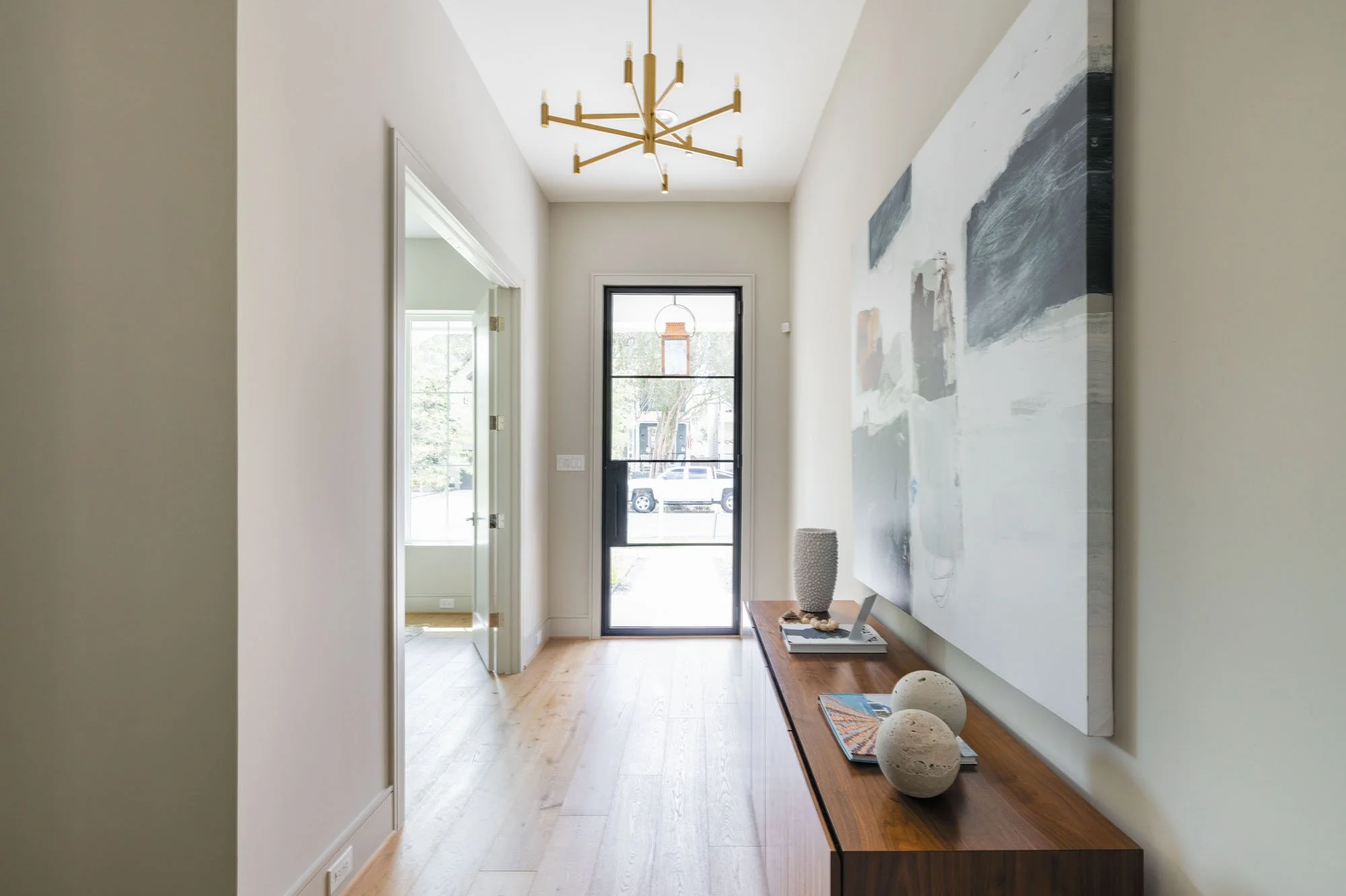 Foyer with black steel-frame glass front door, walnut credenza, and modern brass chandelier