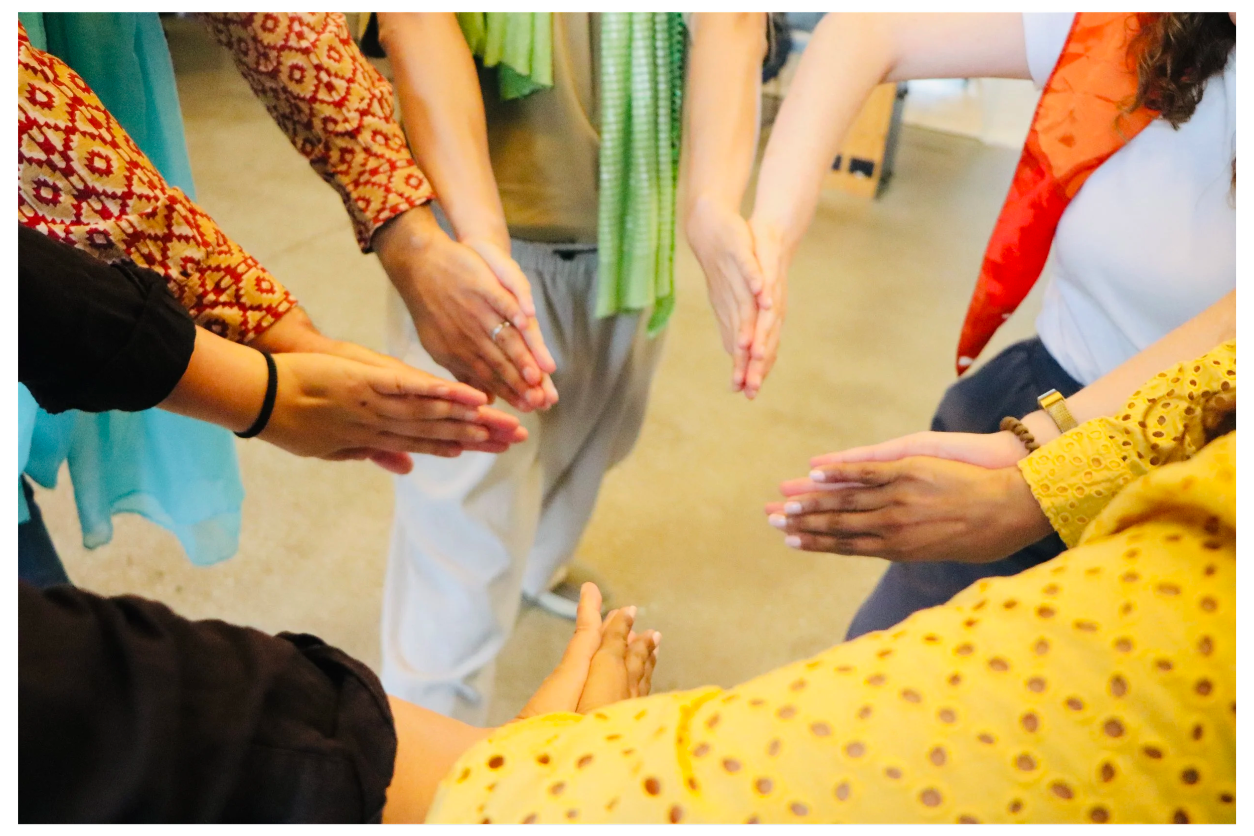Six people standing in a circle with hands together in the middle, as in a group hug or team gesture.