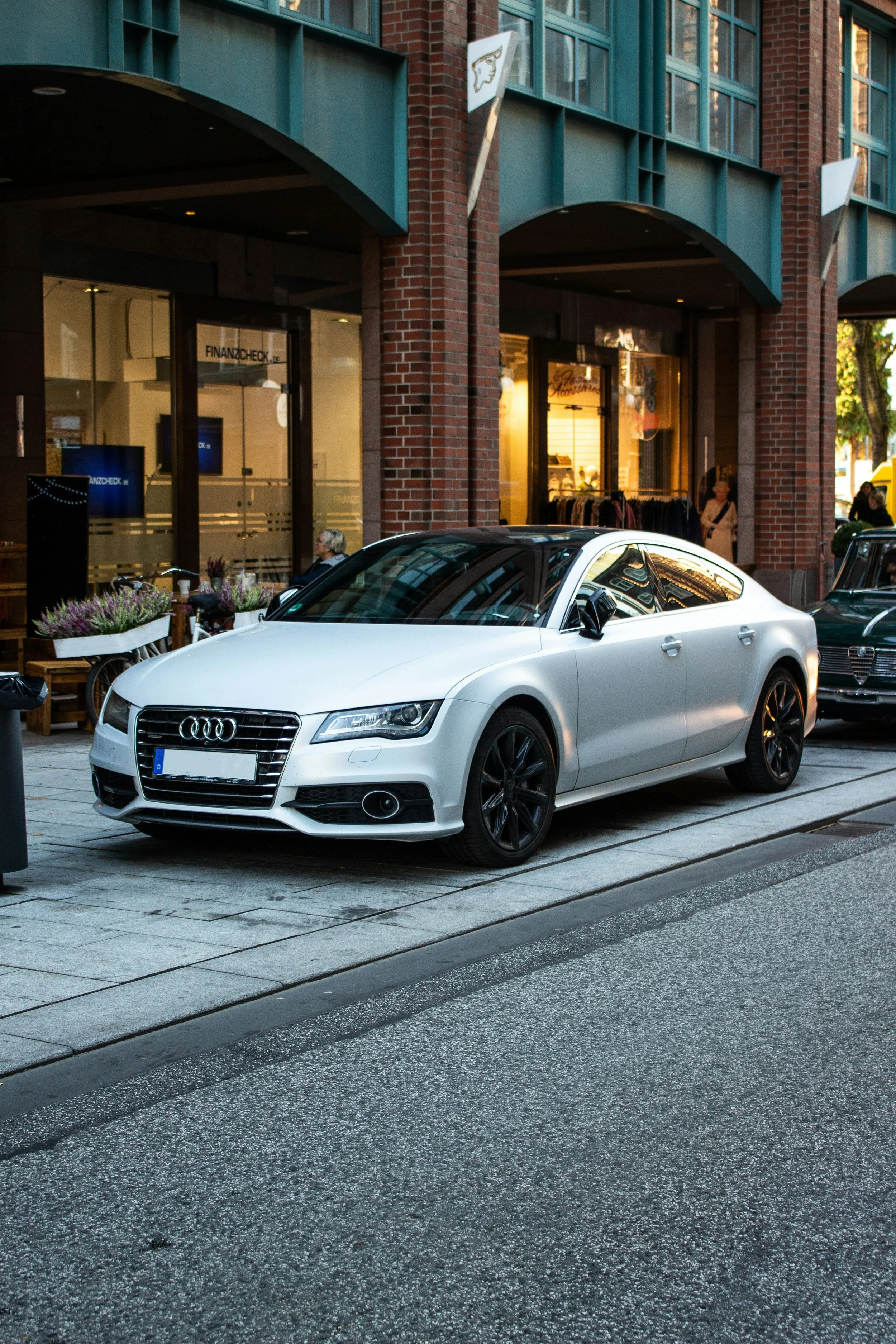 A white Audi car parked on the city street in front of storefronts at sunset.