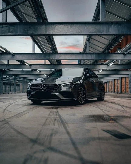 Black Mercedes-Benz car parked in an urban parking garage with metal beams overhead.