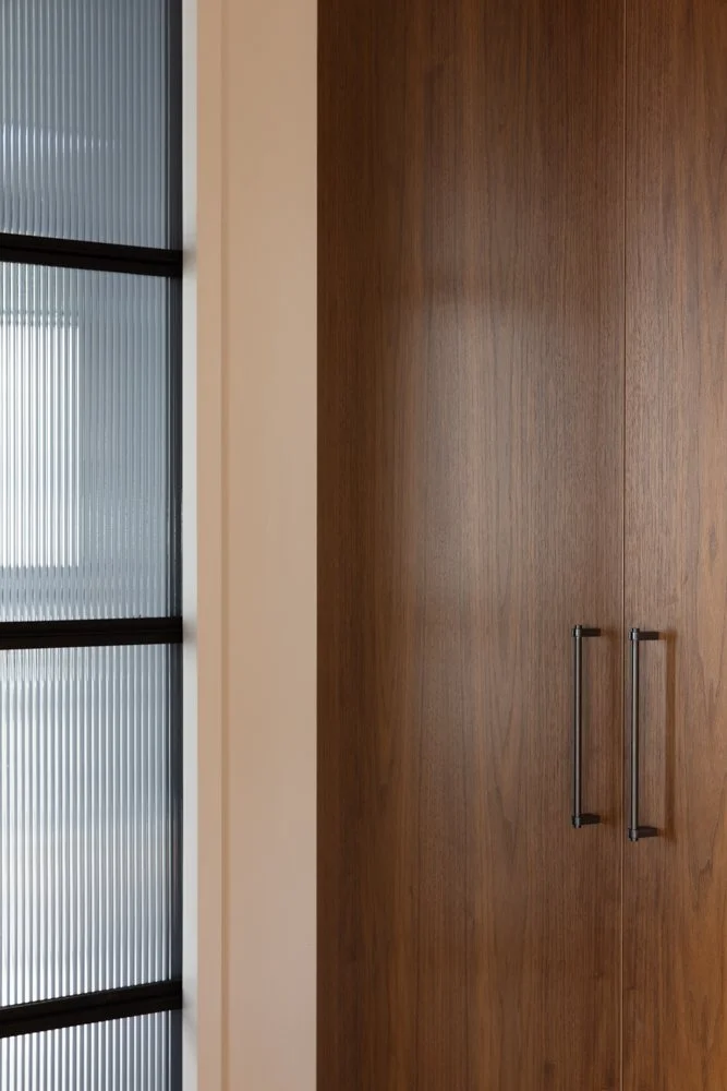 Interior view featuring a wooden cabinet with black handles and a wall with a window or door with translucent ribbed glass panels.