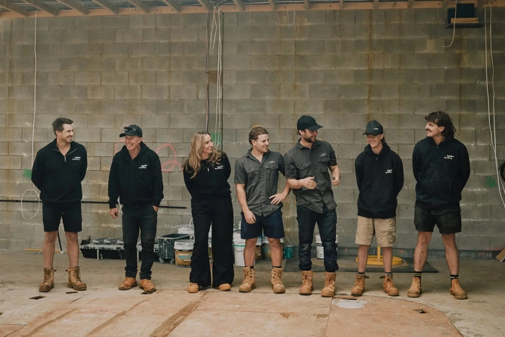 Group of people wearing Layden uniforms standing inside a construction site. All smiling.