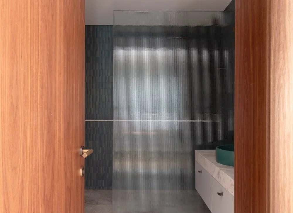 View into a modern bathroom with a wooden door, metallic textured wall, and a white vanity with a green basin
