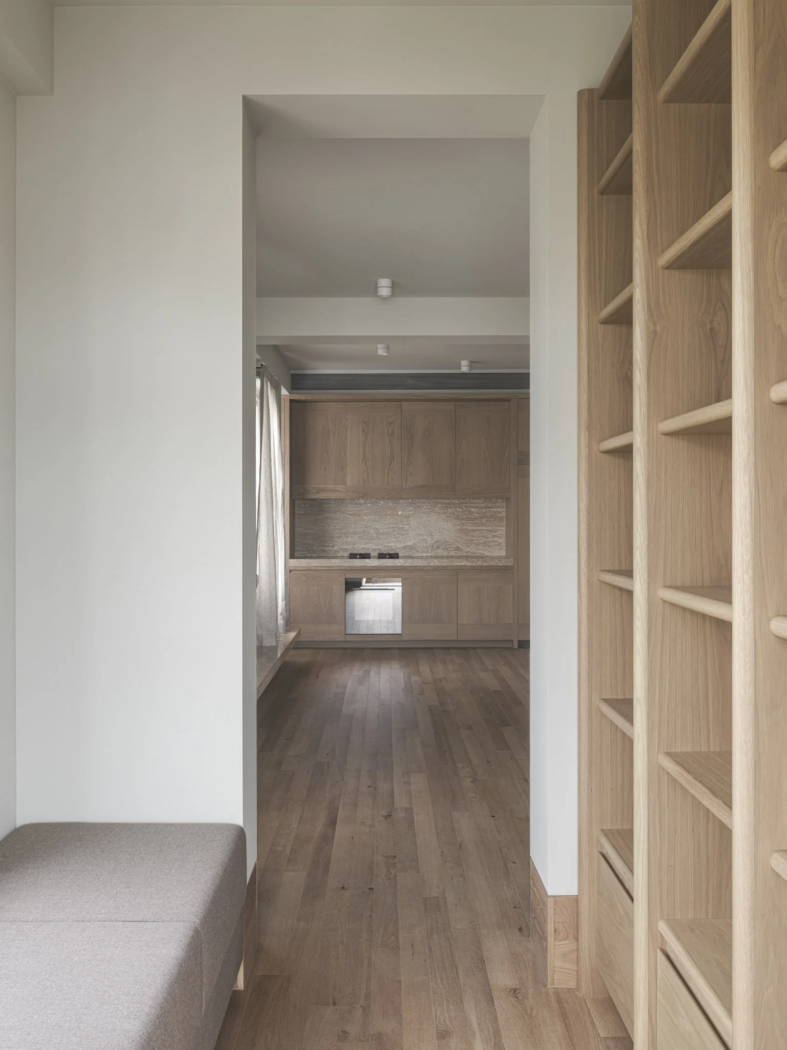 Interior view of a modern home with wood flooring, wood cabinets in the kitchen, and wooden shelving on the right side.
