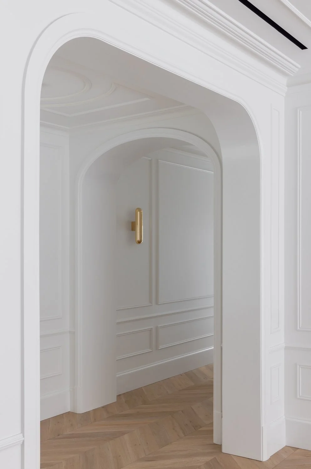 White interior doorway with gold handle, molding details, and light wood herringbone flooring.