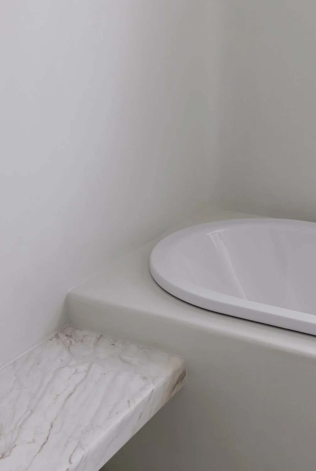 Close-up of a white ceramic bathroom sink with a marble countertop and a simple, white painted wall background.