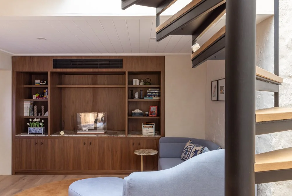 Living room with a blue couch, a wooden bookshelf built into the wall, a spiral staircase with wooden steps and black support, and framed pictures on the wall.
