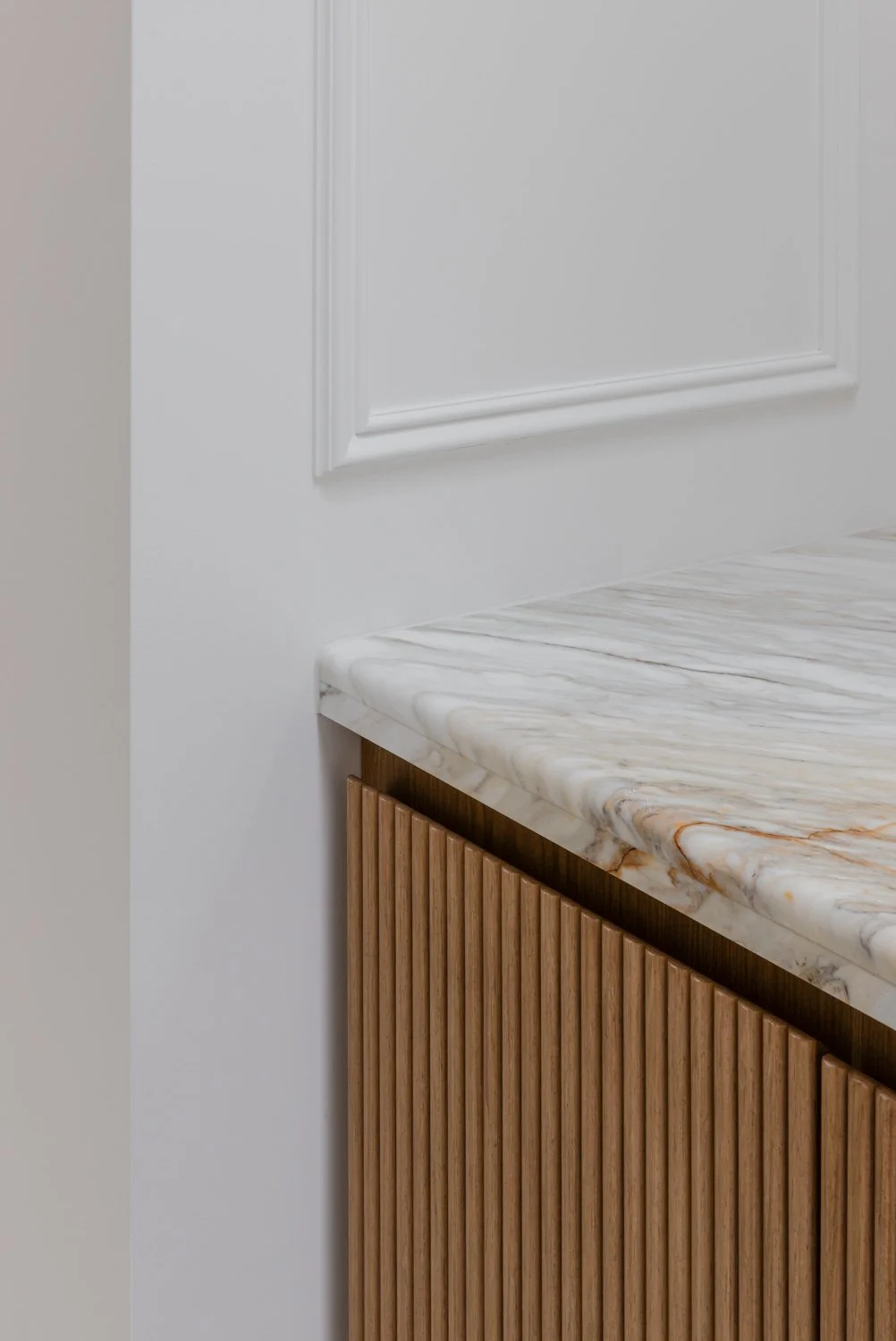 Close-up of a kitchen counter with a marble surface and a wooden cabinet. The background features a white wall with decorative molding.