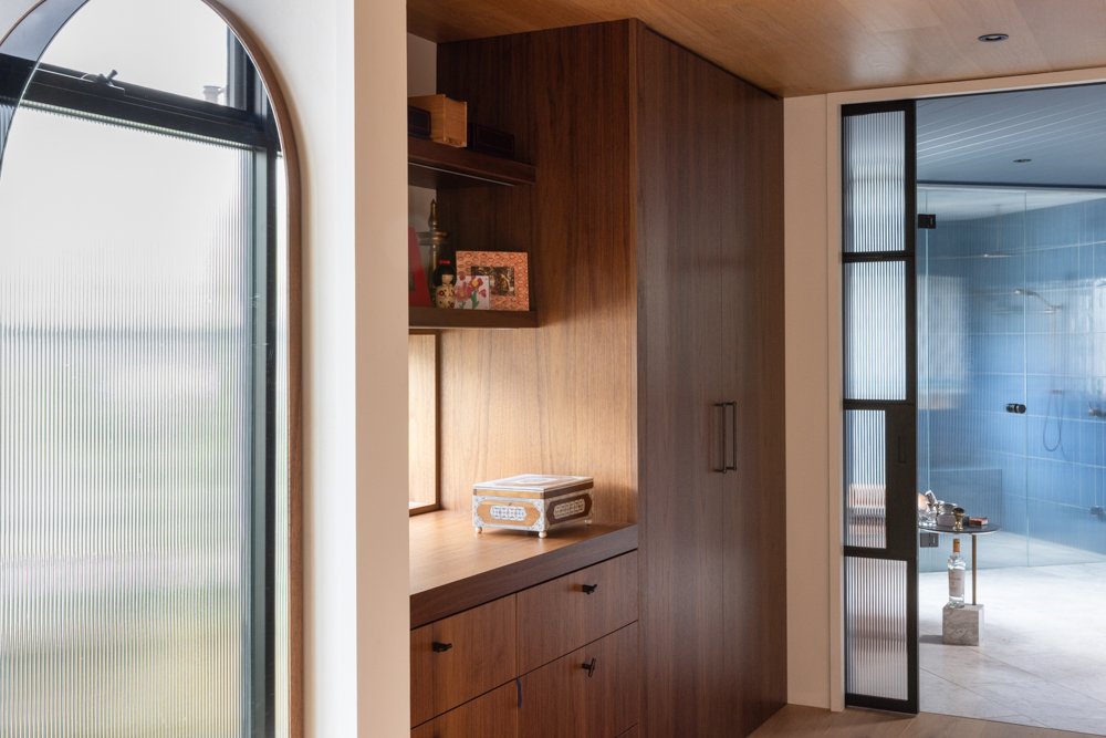 Wood-paneled interior with built-in cabinetry, a small window, and a glass door leading to a modern shower area with blue tiles and a bench.