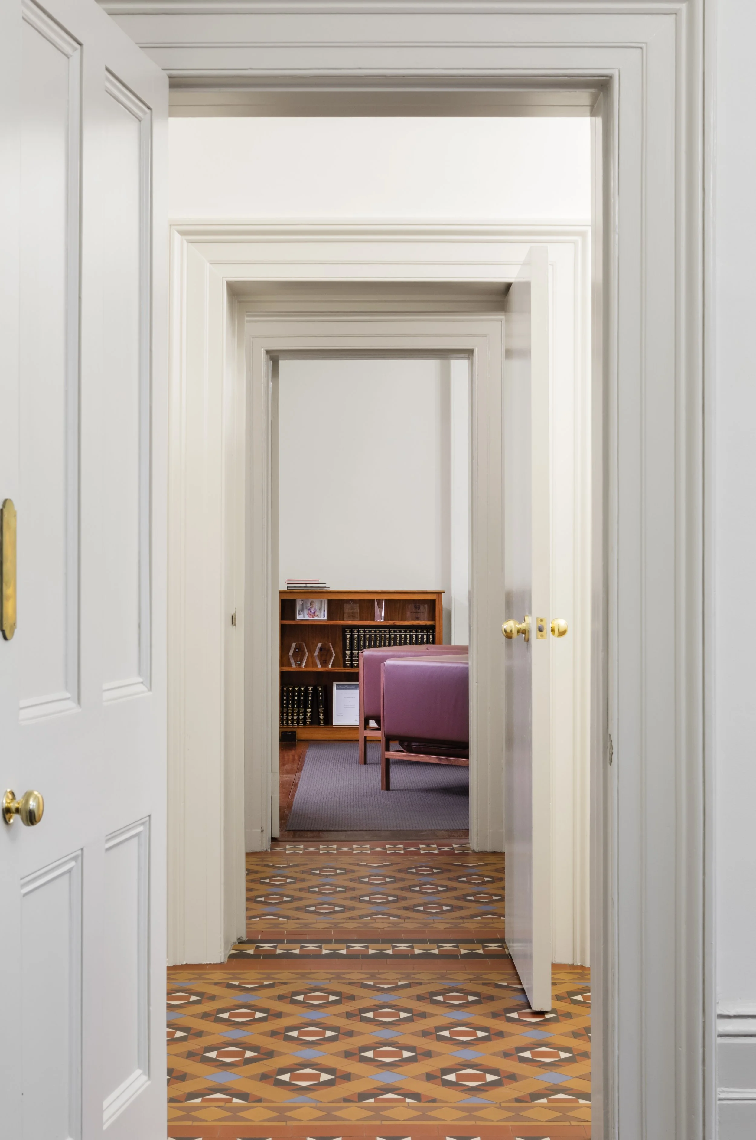 A view through multiple white doorways leading into a room with a purple sofa, a wooden bookshelf, and a bookshelf filled with books.
