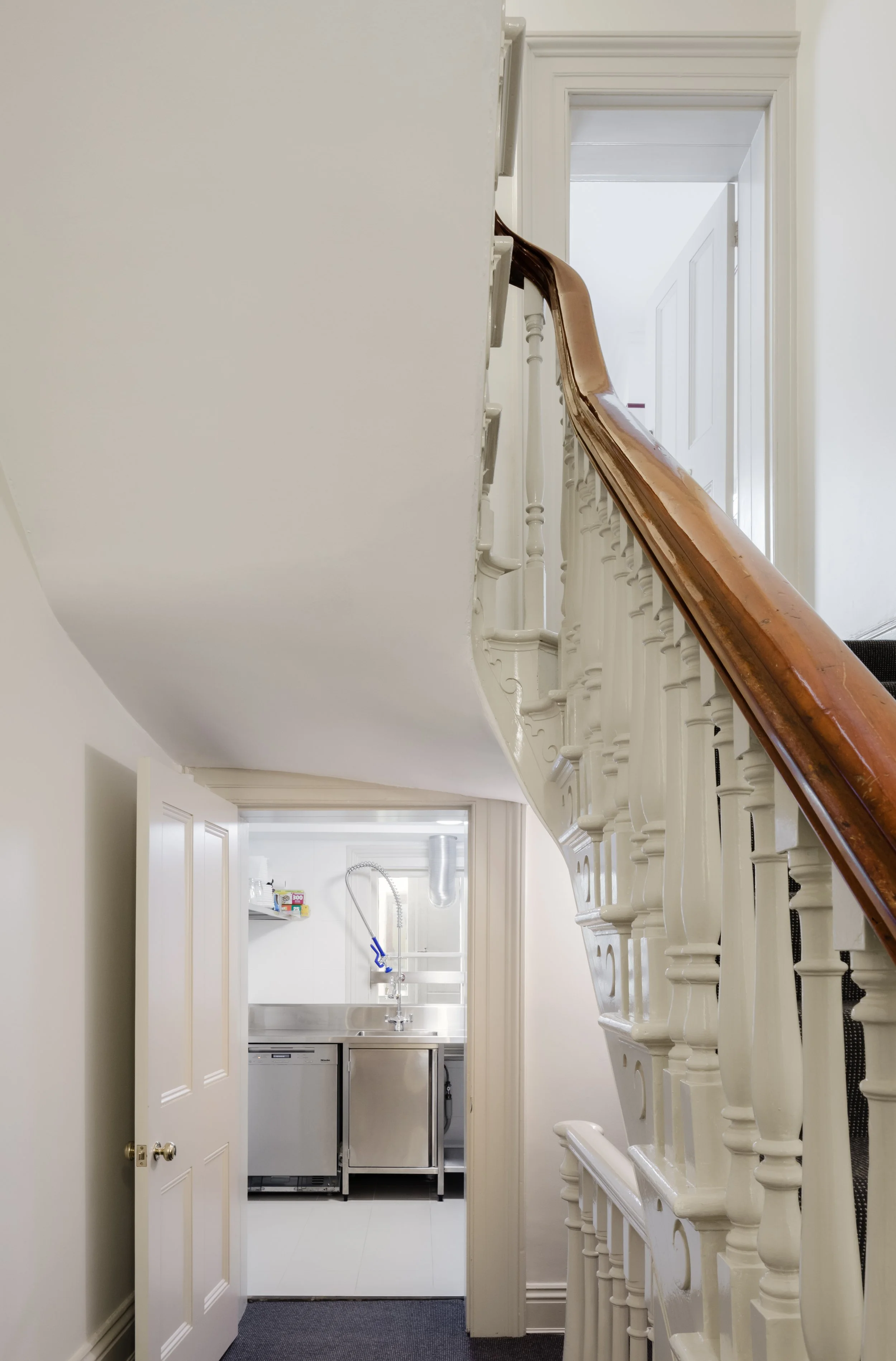 View of a staircase with wooden handrail and white spindles, a partially open door leading to a laundry room with stainless steel appliances, and an air duct and window in the laundry room.