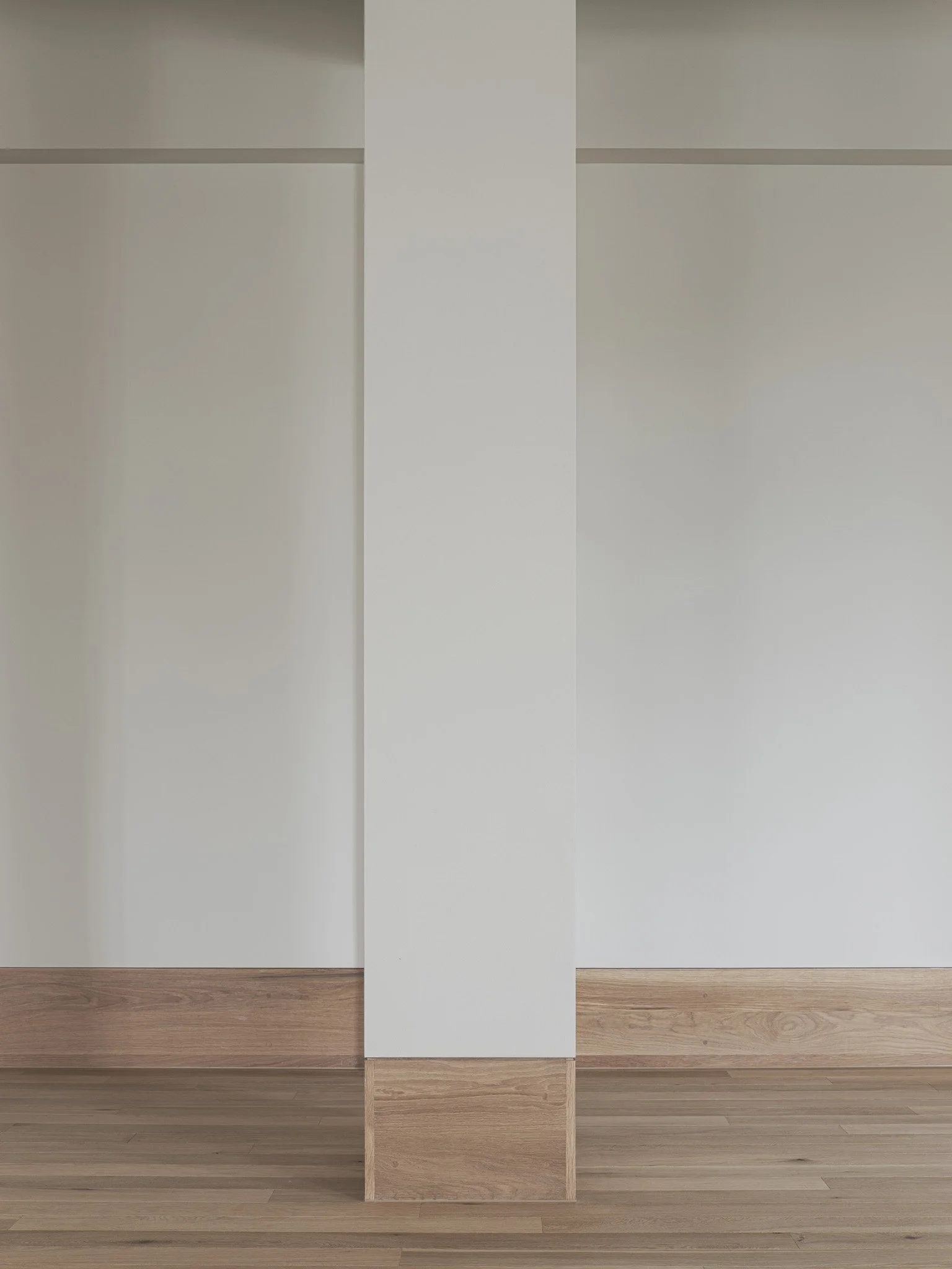 A minimalist interior wall with white panels and natural wood trim and flooring.
