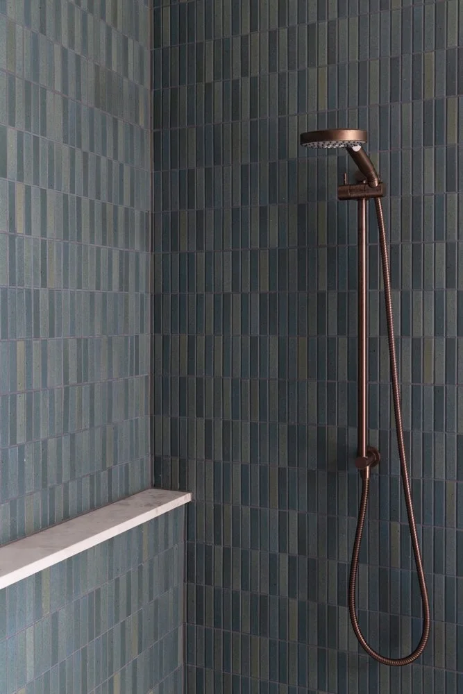 Bathroom shower with green mosaic tile walls, a built-in marble shelf, and a bronze showerhead with a handheld hose.