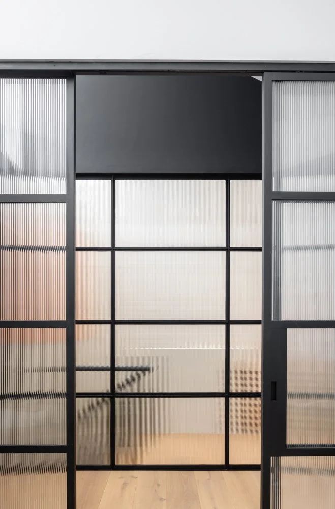 Modern interior space with glass sliding doors with black metal framing, leading to a bright room with a minimalist design.
