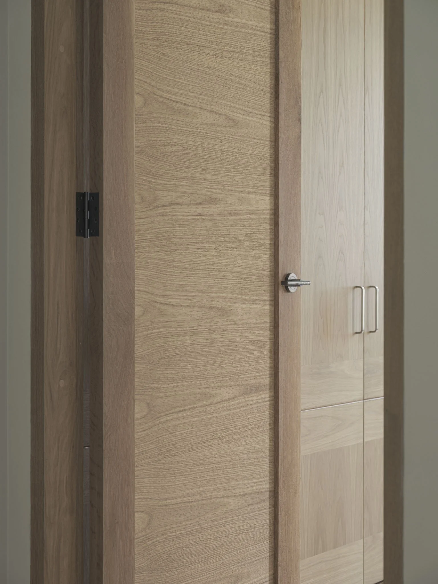 A wooden door slightly open revealing a closet or storage area with light wood cabinetry inside.