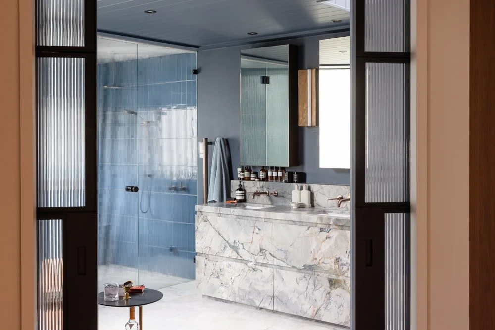 Modern bathroom with blue tiles, marble vanity, and glass shower enclosure.