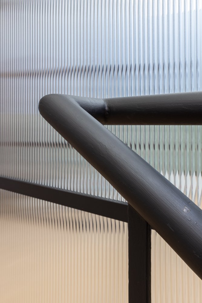 Close-up of a black metal railing with textured translucent glass panels in the background.