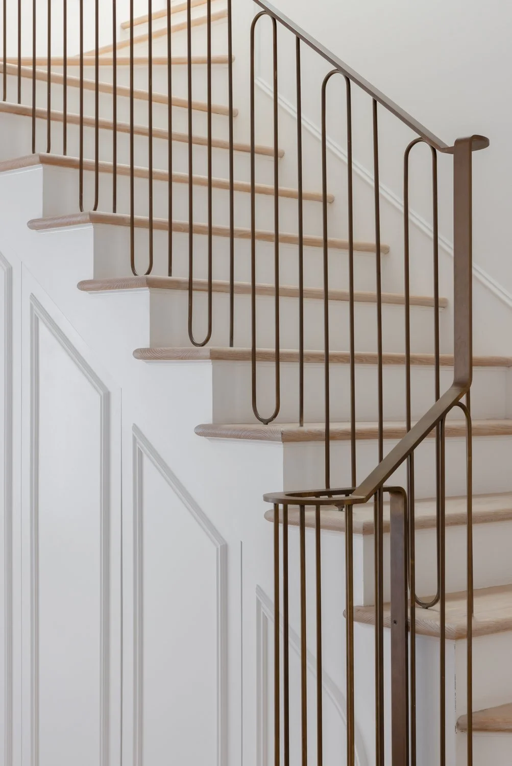 Interior staircase with white paneled wall, wooden steps, and black metal railing.