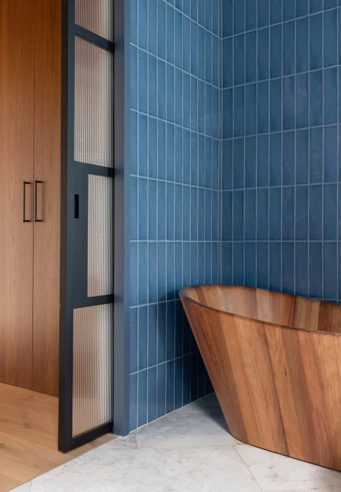 Wooden bathtub next to a blue tiled wall in a modern bathroom.