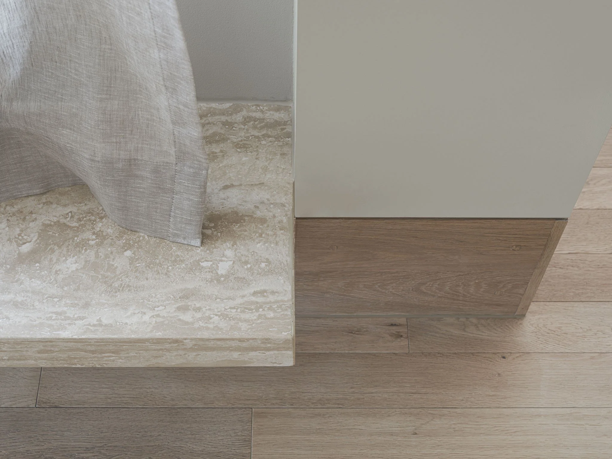 Close-up of a corner with a beige marble surface, gray fabric curtain, light beige wall, and wooden floor and trim.