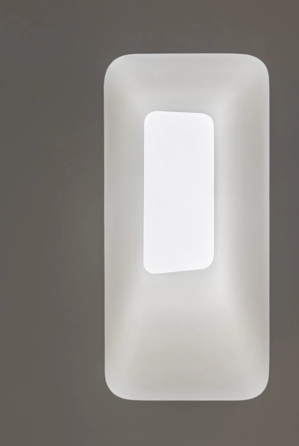 Close-up of a minimalist, modern, white light fixture with a rectangular shape and rounded edges, mounted on a plain wall.