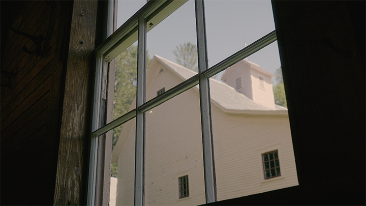 View of an old white house through a window framed with wood and metal muntins.